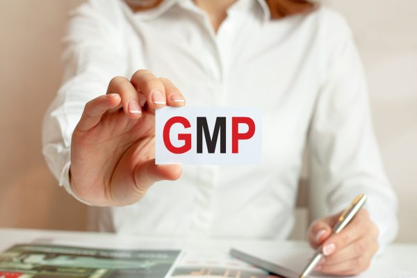 A woman in a white shirt holds a piece of paper with the text: GMP. Business concept for companies. GMP - short for good manufacturing practice.